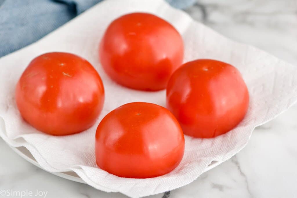 four tomatoes with their tops removed overturned on a paper towel lined plate