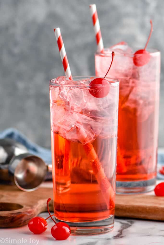 two high ball glasses filled with Shirley Temple drink and topped with a cherry and stripped straws