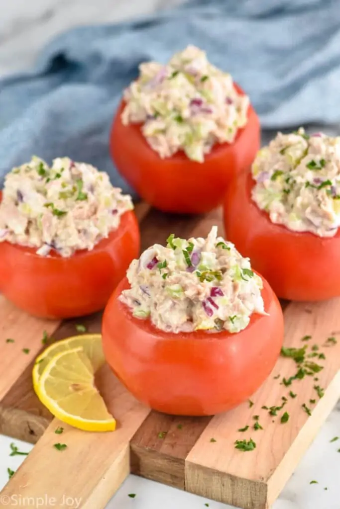 four tuna stuffed tomatoes on a wood cutting board, garnished with fresh parsley