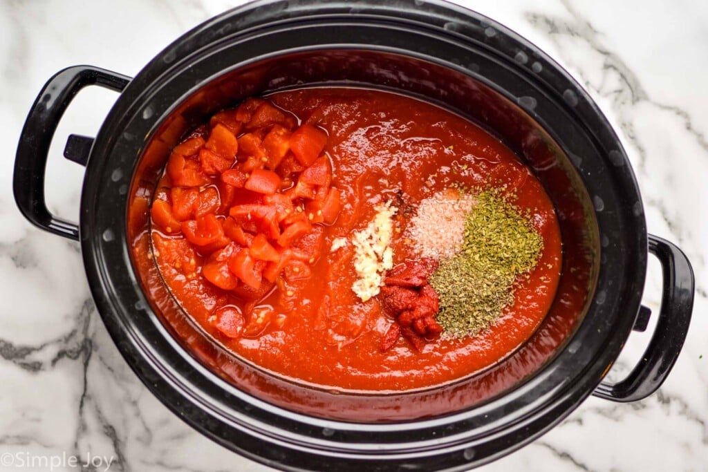 overhead of a slow cooker full of ingredients to make spaghetti sauce before they are mixed together