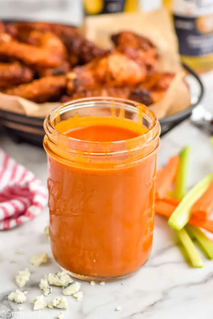 mason jar with buffalo sauce recipe with wings in the background