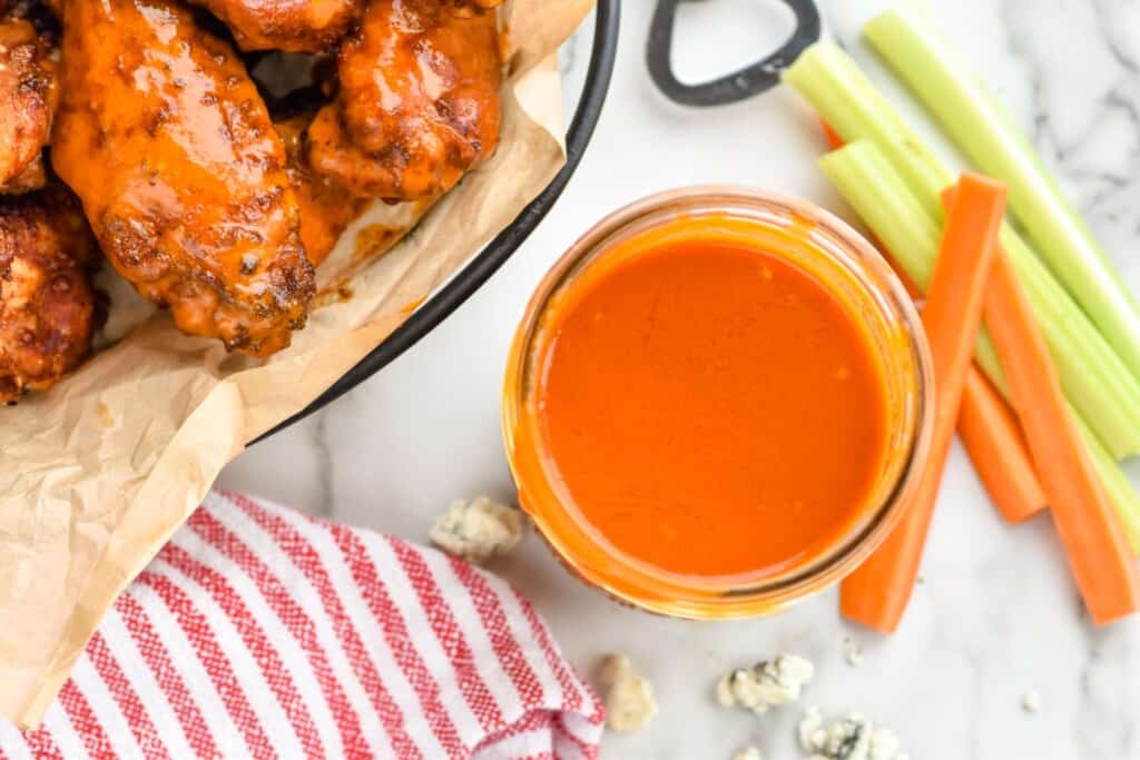 overhead of a mason jar with buffalo sauce with a basket of wings next to it