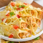 a plate of chicken taquitos topped with lettuce, tomatoes, and shredded cheese