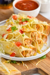 a plate of chicken taquitos topped with lettuce, tomatoes, and shredded cheese