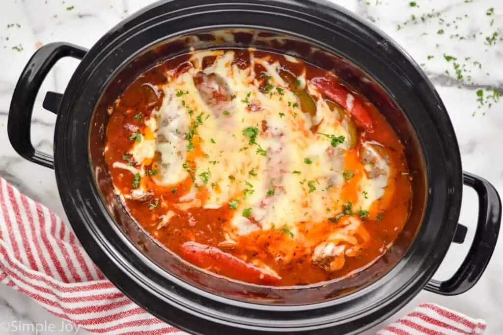overhead of a crockpot full of red sauce with sausages that have cheese melted over them
