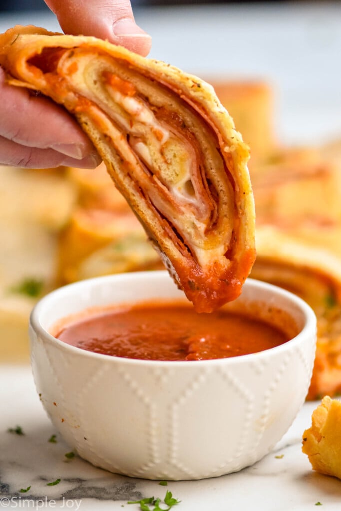 piece of a stromboli being dipped in sauce