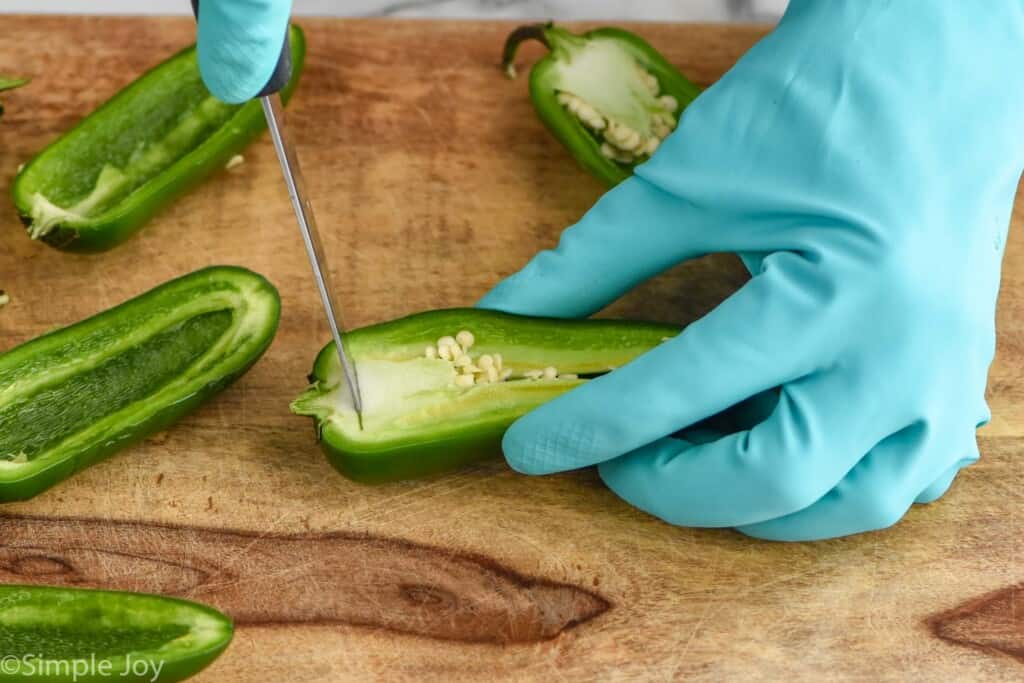 close up of a gloved hand cutting the seeds out of a jalapeno half
