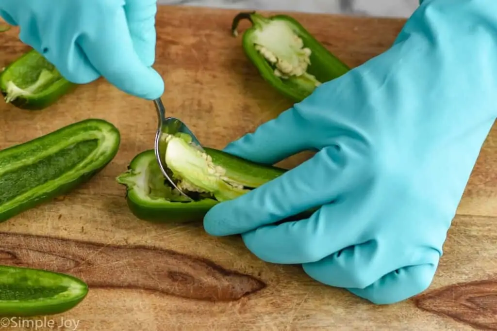 close up of a gloved hand removing the ribbing of a jalapeno that has been cut in half with a spoon