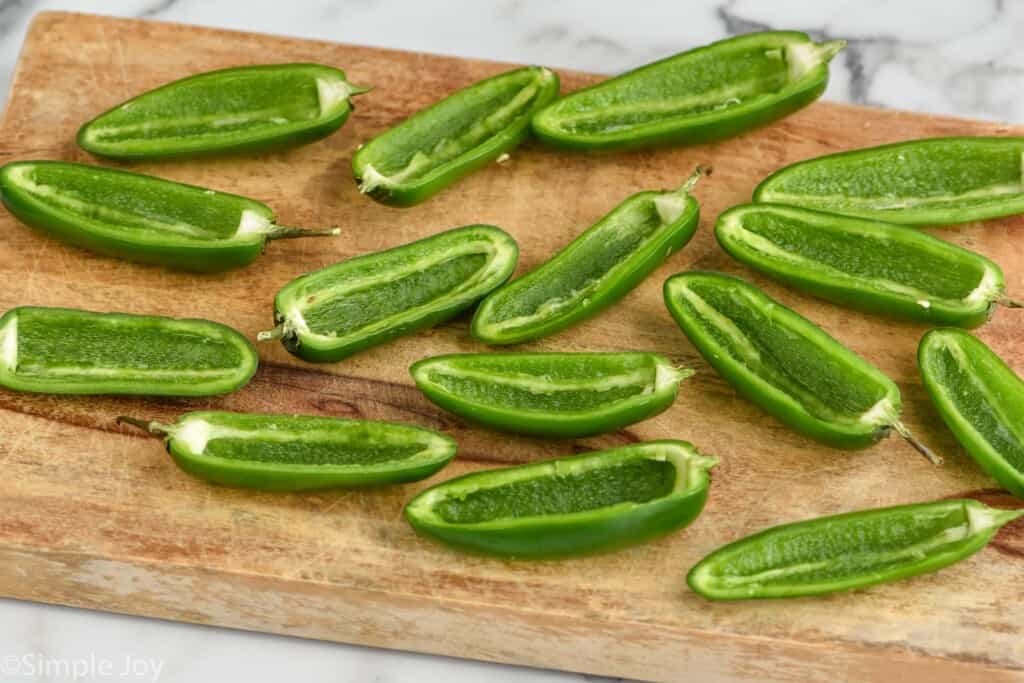 cutting board with jalapeno halves that have had their seeds and ribbing removed on it