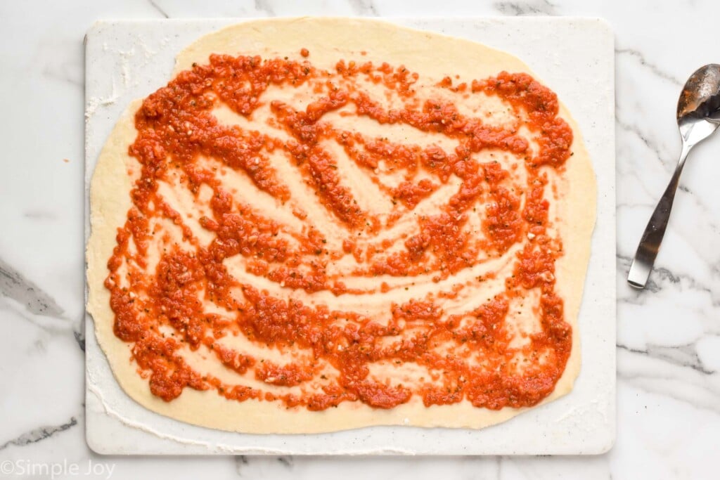 overhead of dough rolled into a rectangle with pizza sauce on it
