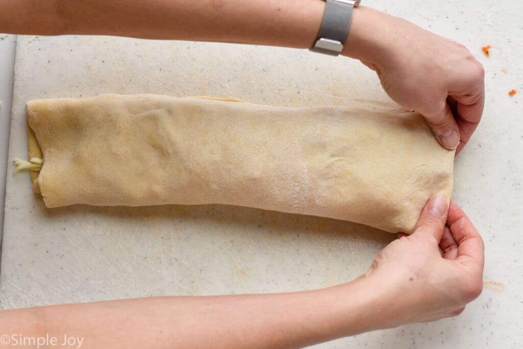 overhead of hands pinching the ends of a rolled up stromboli