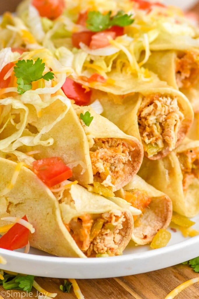 close up of a plate of taquitos topped with lettuce, tomatoes, and cheese