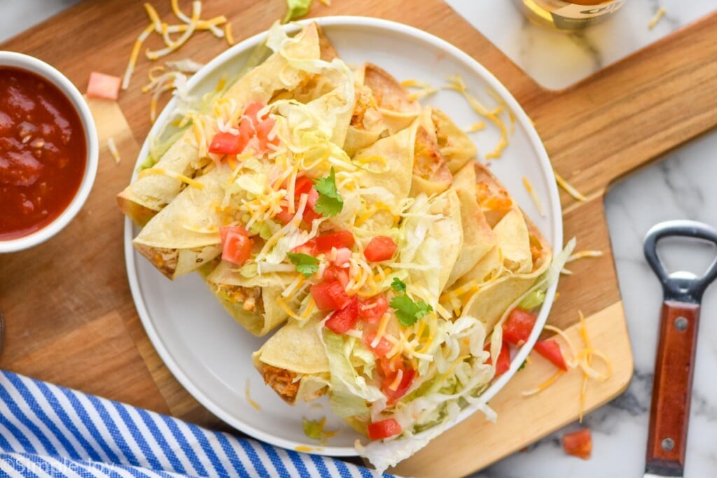 overhead of a plate of taquitos that are topped with lettuce, tomatoes, and cheese