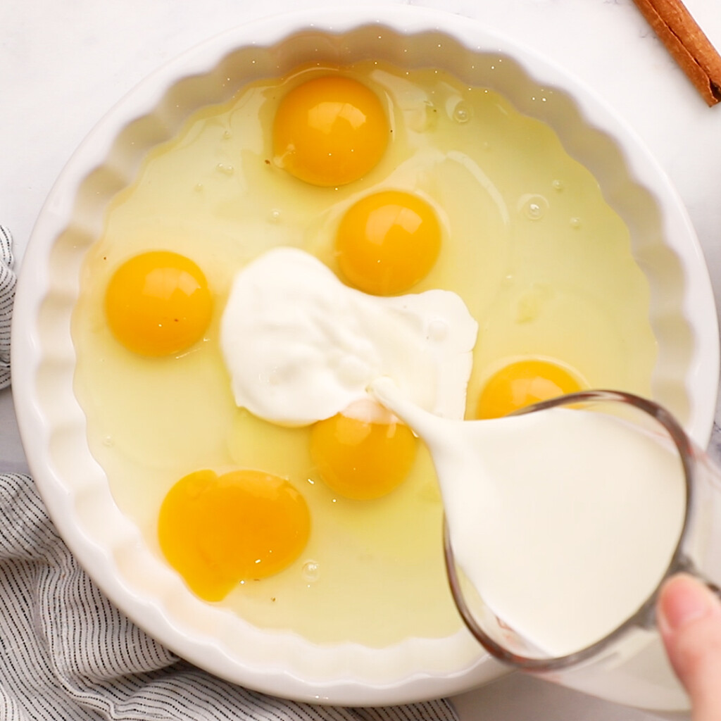 half and half being poured into a pie plate with eggs in it