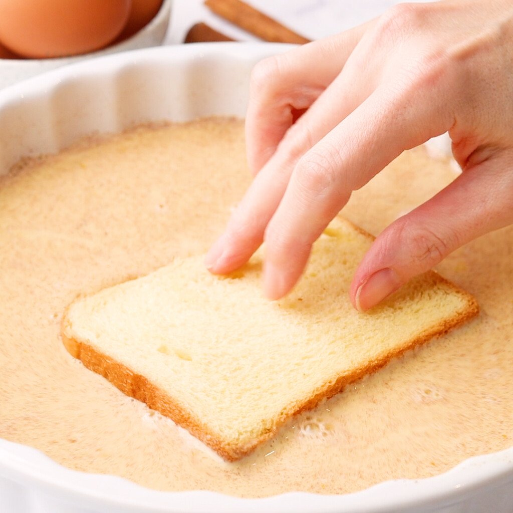 bread being soaked in batter to make French toast