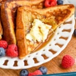 pinterest graphic of four triangles of French toast recipe sitting on a white plate with butter, syrup, and fresh berries