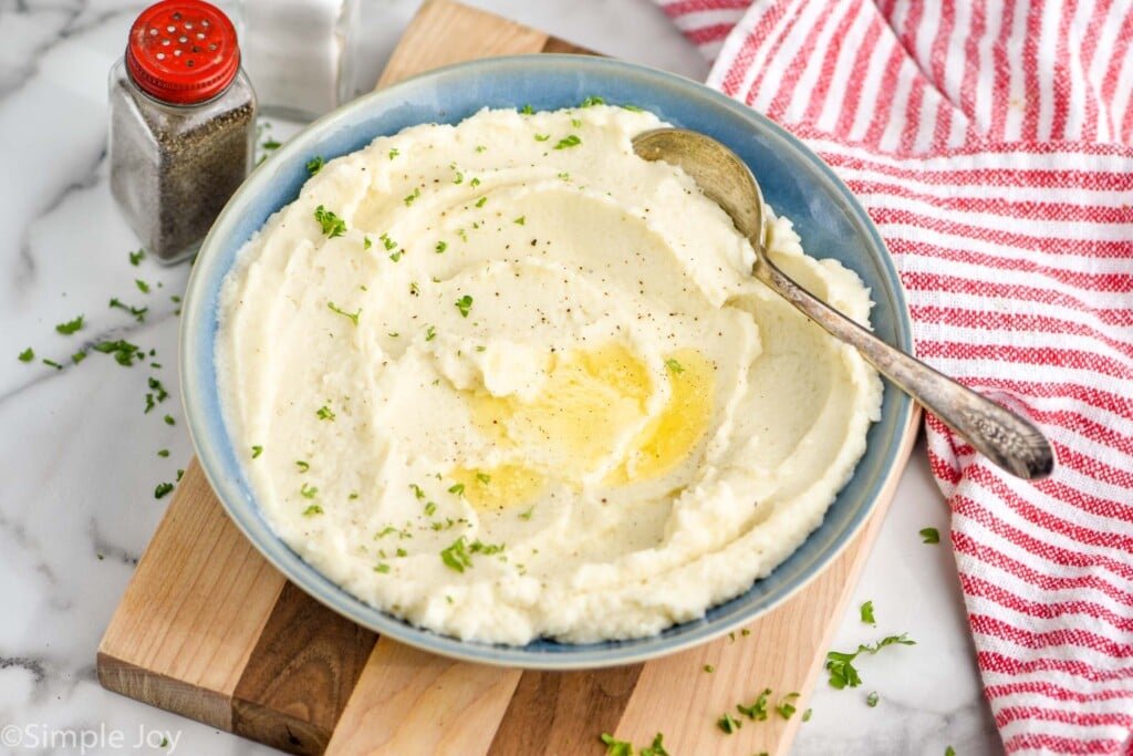 side view of a bowl of cauliflower mash garnished with parsley, pepper and butter