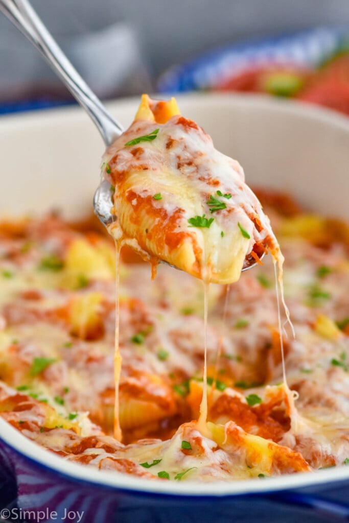 a stuffed shell being spooned out of a casserole dish