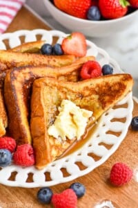 four triangles of French toast recipe sitting on a white plate with butter, syrup, and fresh berries