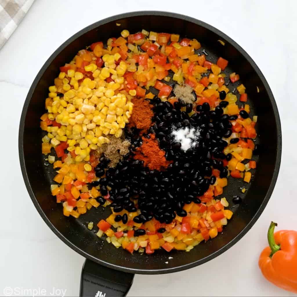 overhead of vegetables, beans, corn, and spices sautéing in a frying pan