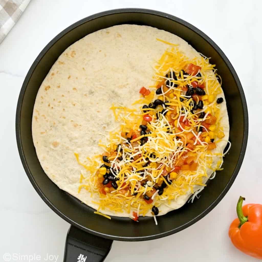overhead of a tortilla in a skillet with cheese and vegetables on one side