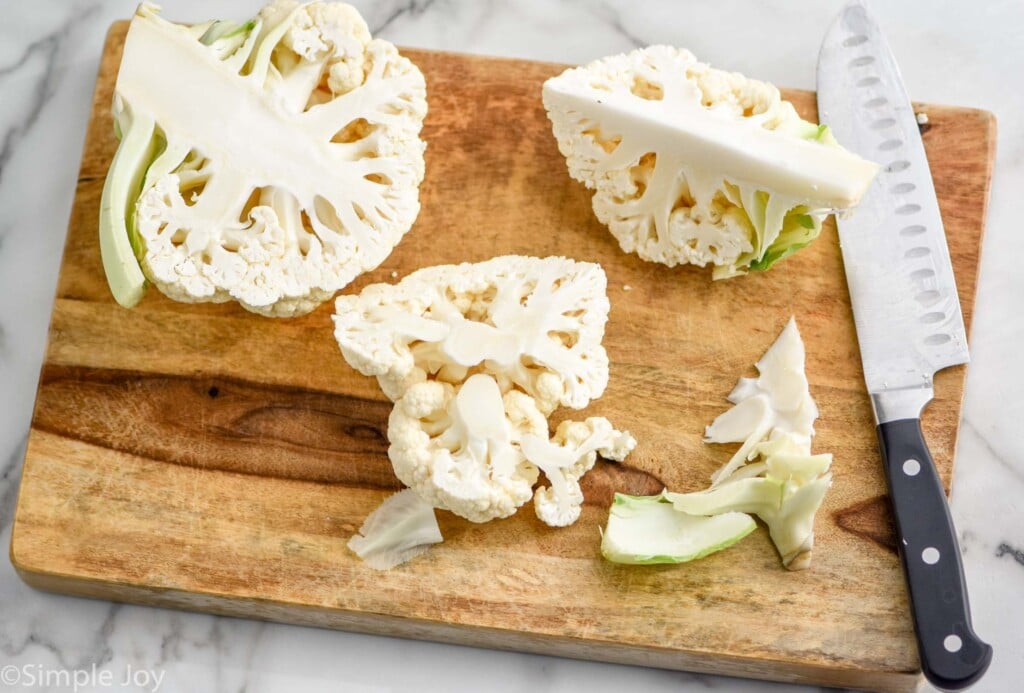 cauliflower that has been cut in half, then cut in fourths, and the core removed from one fourth on a cutting board