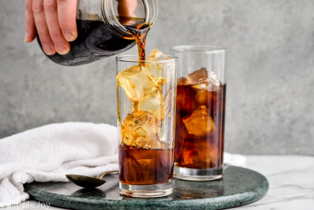 pouring cold brew coffee over ice in a tall tumbler