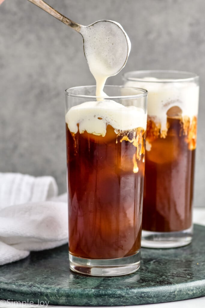 pouring cold foam over cold brew coffee