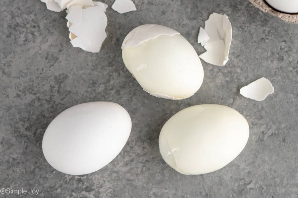 overhead of three hard boiled eggs being peeled