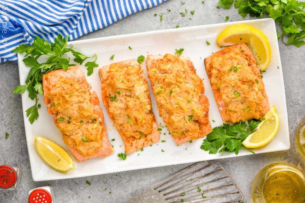 overhead of four pieces of salmon stuffed with crab on a platter with parsley and lemon wedges