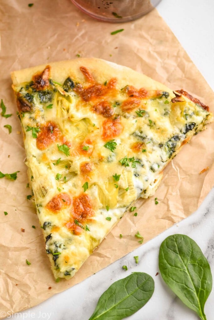 a piece of spinach and artichoke pizza sitting on parchment paper