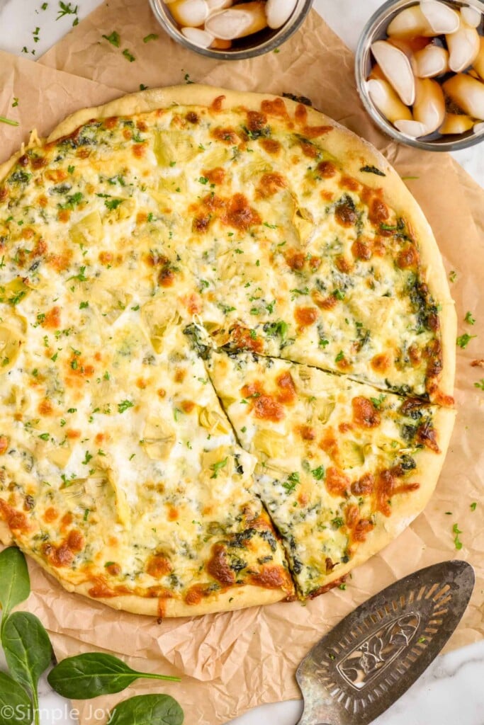 overhead of a spinach artichoke pizza with a piece cut but not taken out