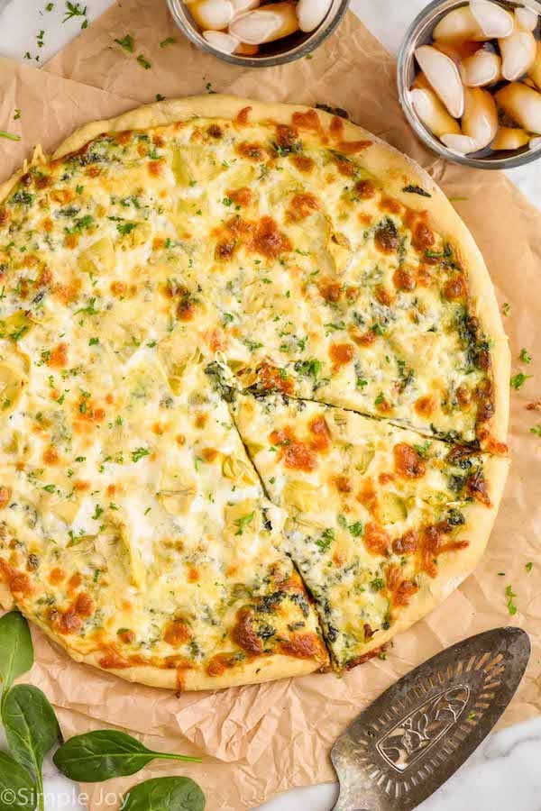 overhead of a spinach artichoke pizza with a piece cut but not taken out