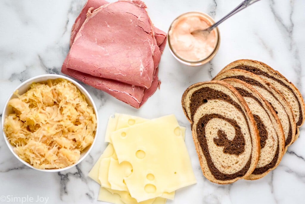 overhead of the ingredients for a Reuben Sandwich - sauerkraut, corned beef, Swiss cheese, Russian dressing, and pumpernickel rye bread