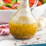 pinterest graphic of italian dressing in a salad dressing container in front of a big white serving bowl full of salad