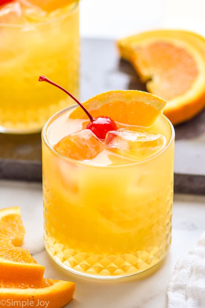 amaretto stone sour in a tumbler with ice, an orange slice, and a cherry