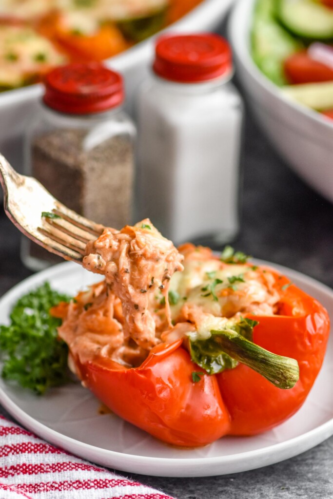 chicken stuffed pepper recipe on a plate with a fork dishing up the cheesy goodness