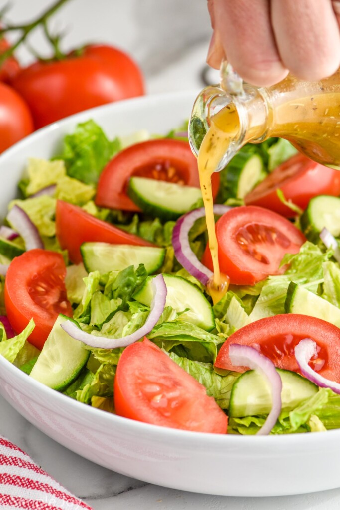 homemade italian dressing being poured over salad