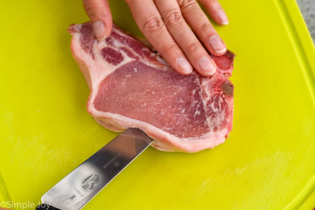 a pork chop on a cutting board with a knife going in the side to make stuffed pork chops