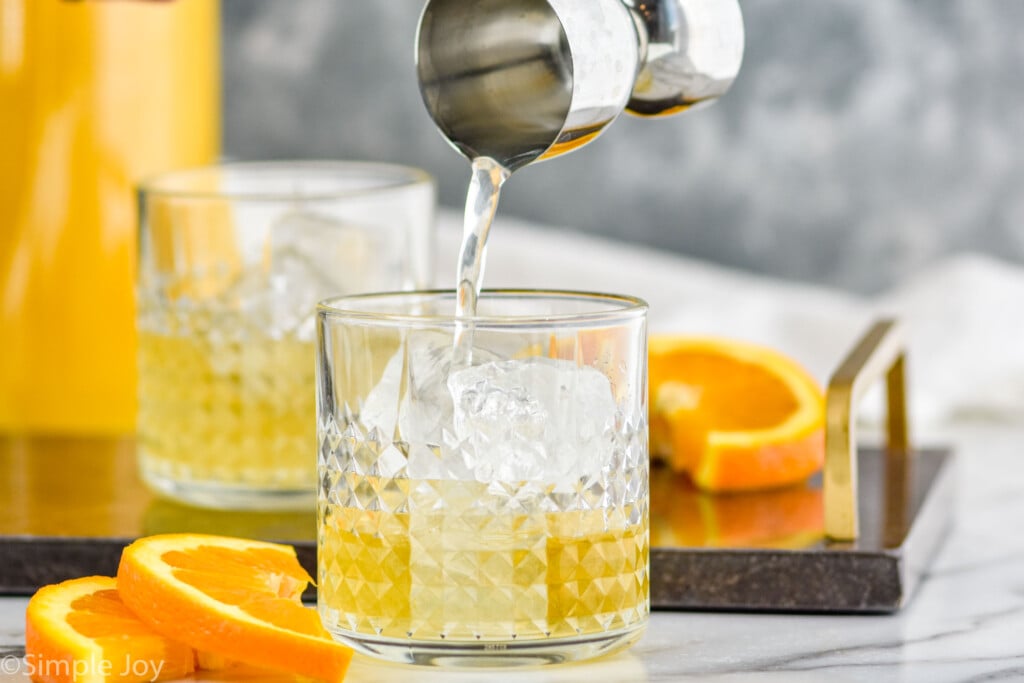 sour mix being poured into a tumbler with ice