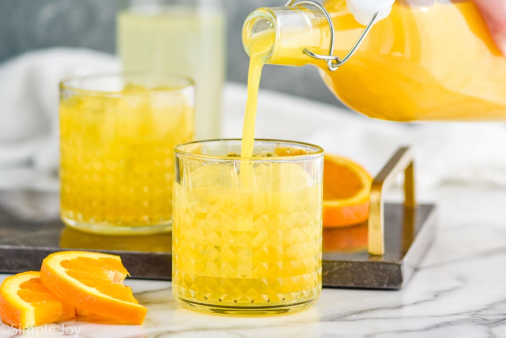 orange juice being poured into a cocktail