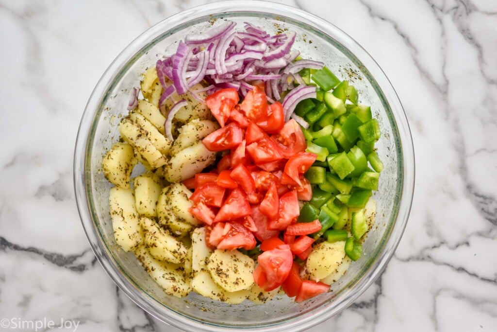 overhead of a bowl of seasoned potatoes, cut up bell peppers, red onions, and tomatoes for Italian potato salad