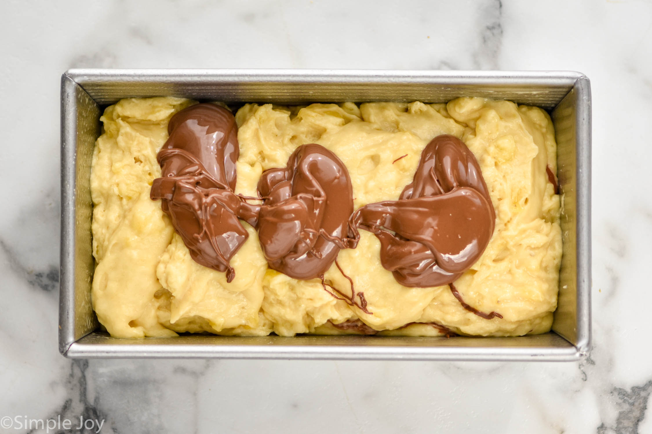 overhead of banana bread batter with three drops of Nutella in it