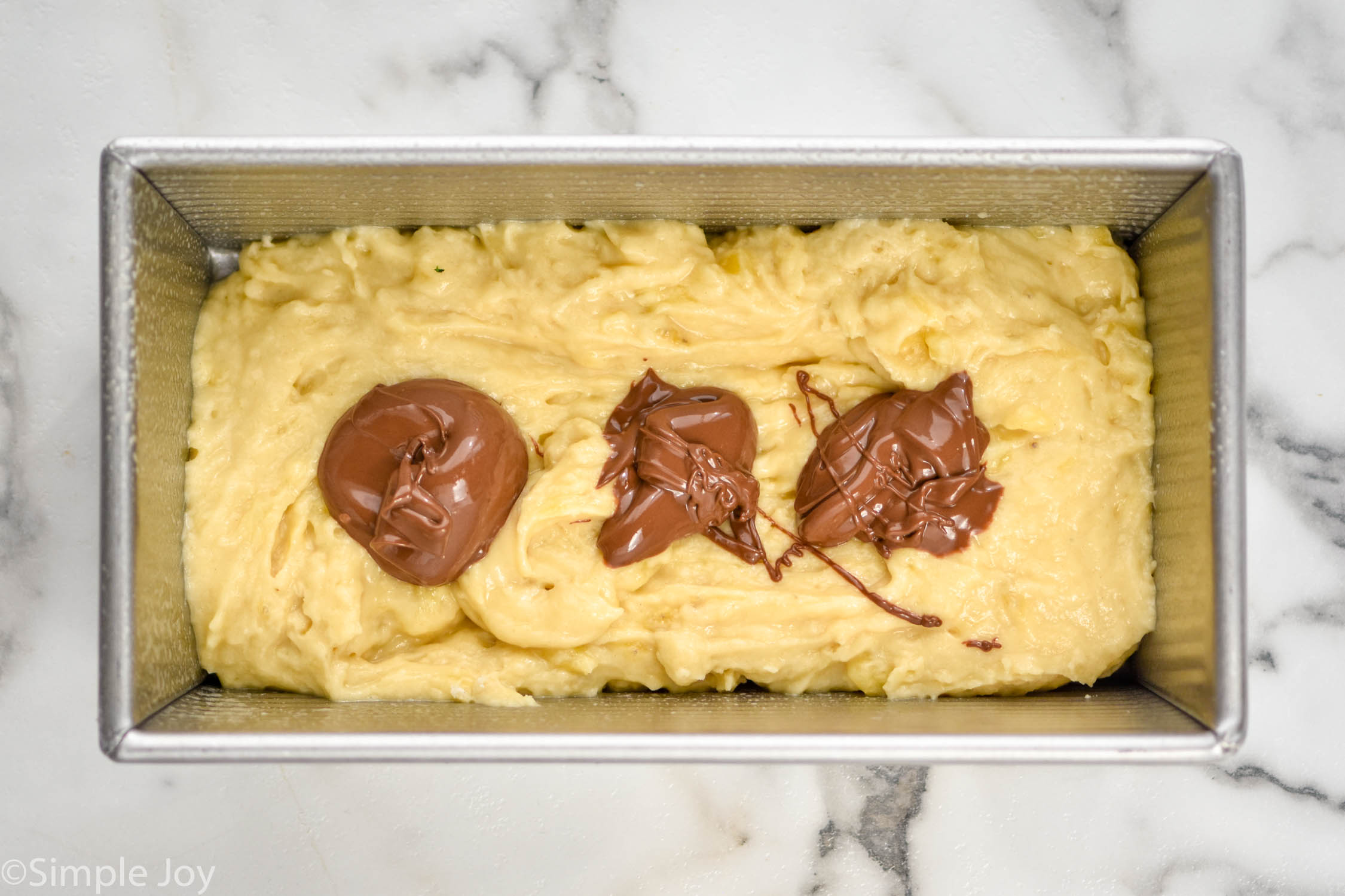 overhead of banana bread batter with three drops of Nutella in it