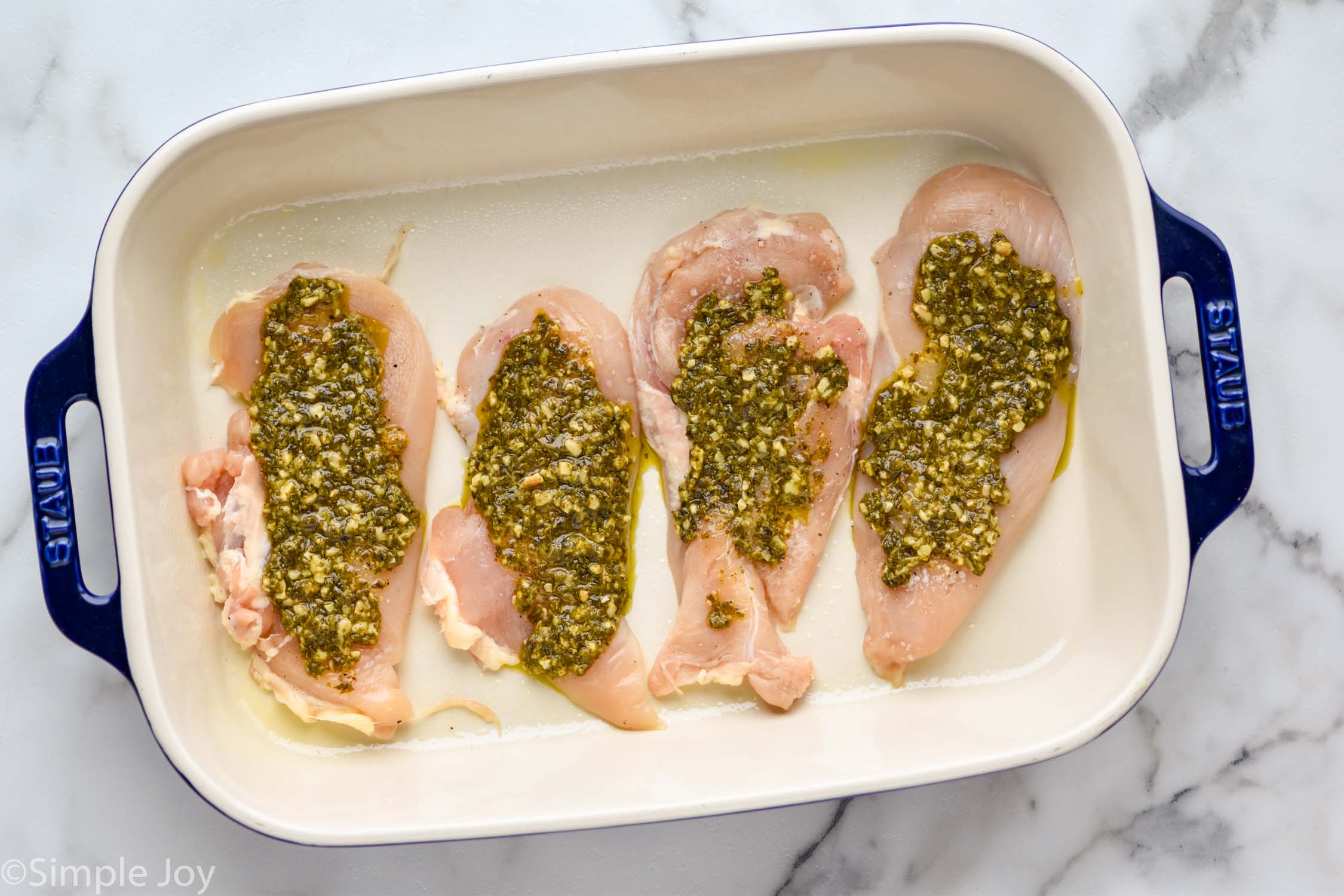 overhead of a baking dish will four chicken cutlets topped with pesto