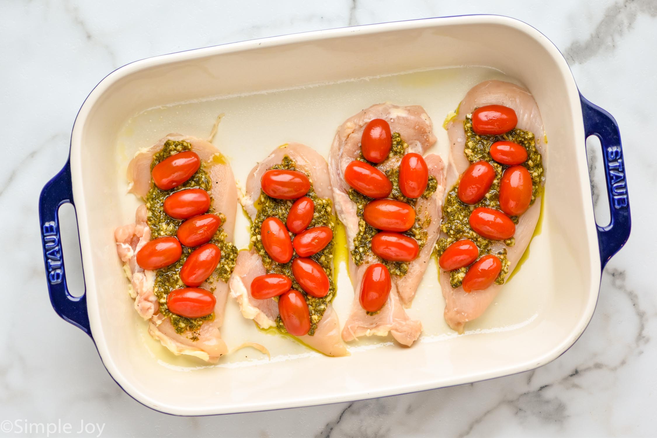 overhead of a baking dish will four chicken cutlets with pesto and halved cherry tomatoes