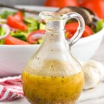 italian dressing in a salad dressing container in front of a big white serving bowl full of salad - 8