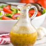 italian dressing in a salad dressing container in front of a big white serving bowl full of salad