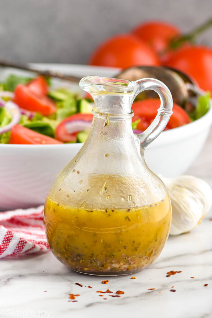 italian dressing in a salad dressing container in front of a big white serving bowl full of salad