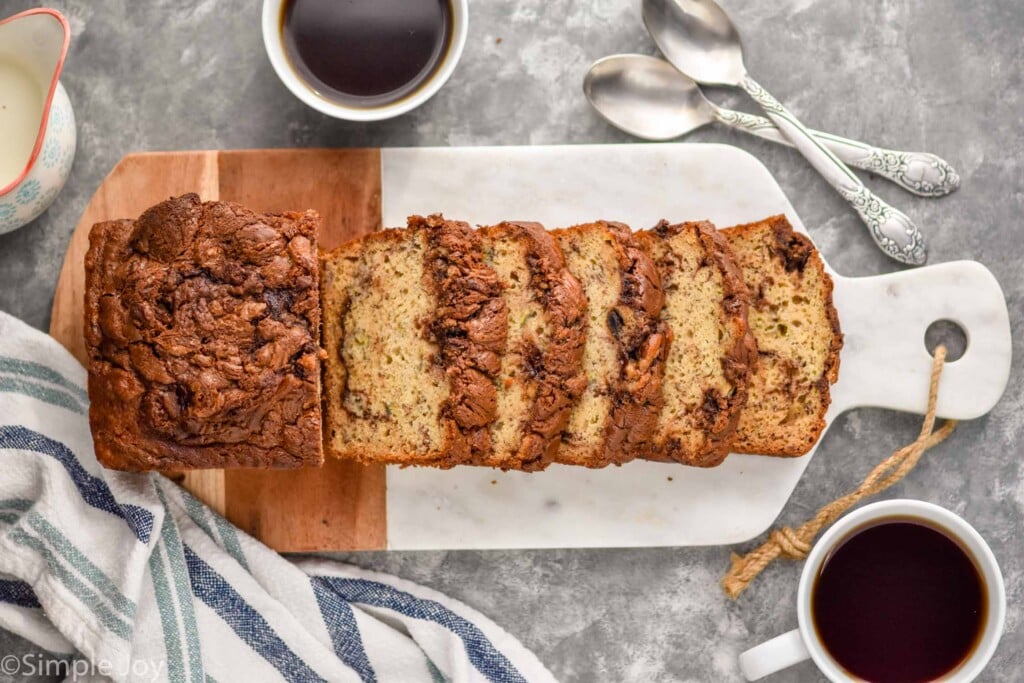 overhead of Nutella banana bread cut up on a cutting board next to two cups of coffee